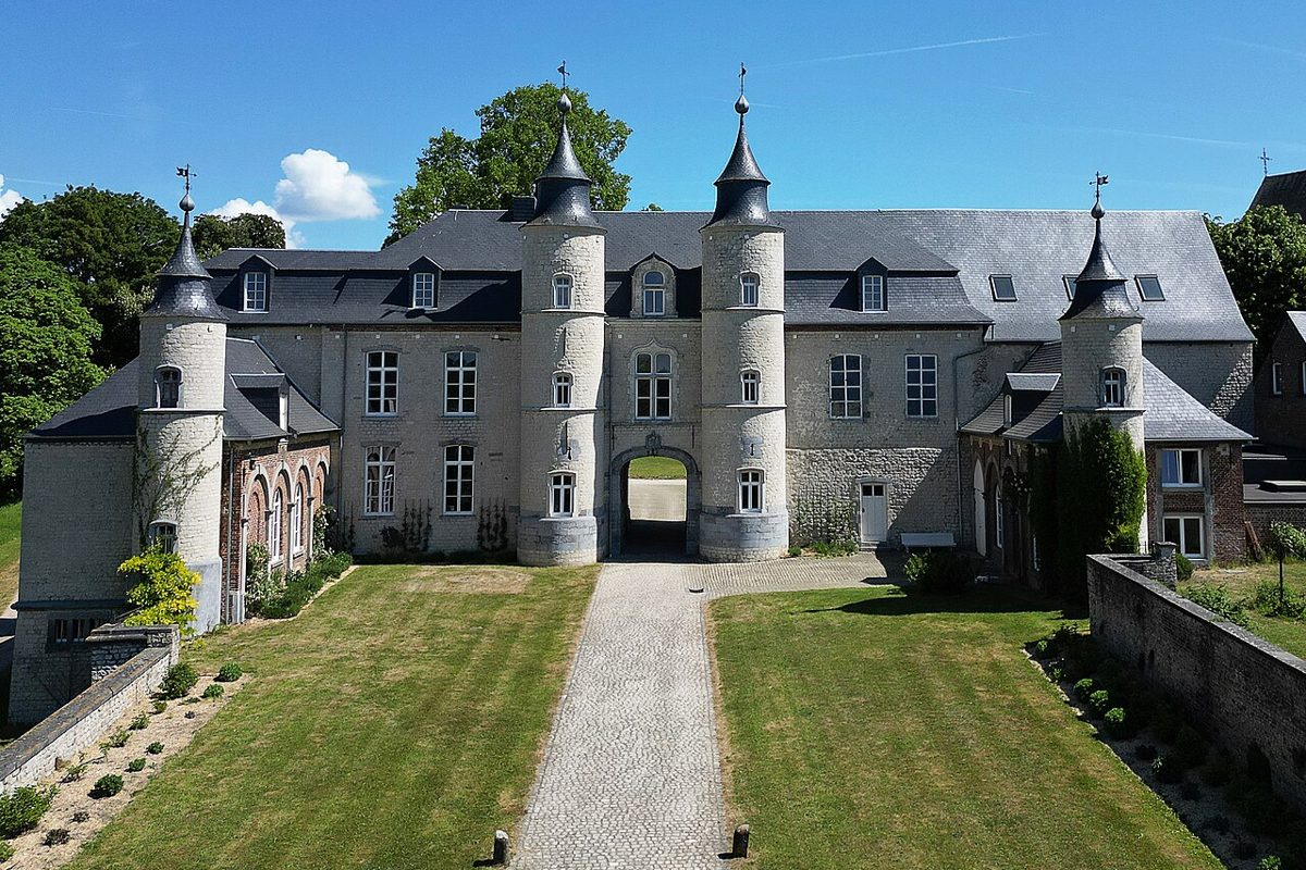 La façade du château d'Houtain-le-Val, ses tours rondes et son porche d'entrée, sous un ciel bleu